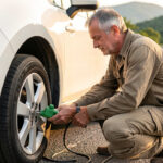 Vérifications avant de prendre la route en voiture : les 9 points essentiels Un homme vérifie les pneus et les niveaux de sa voiture avant de prendre la route, sous une douce lumière matinale.